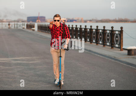 Attraente uomo sorridente a cavallo su blue kick scooter sul tramonto. Foto Stock