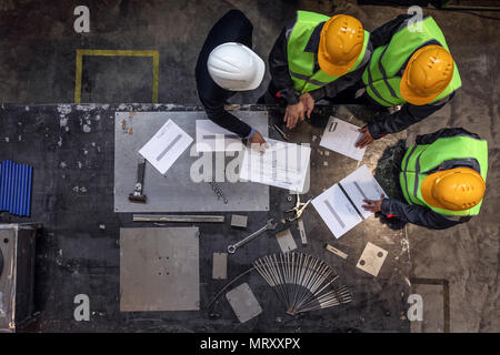 Lavoratori e manager in caschi di sicurezza di lavoro con documenti in fabbrica Foto Stock