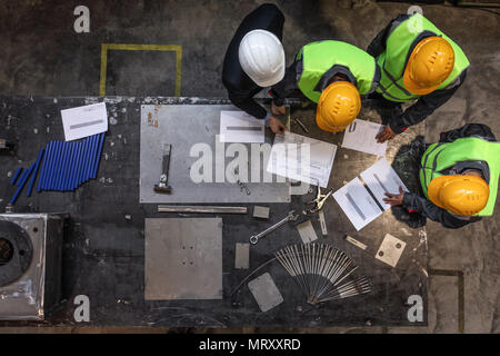 Lavoratori e manager in caschi di sicurezza di lavoro con documenti in fabbrica Foto Stock