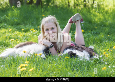 Sorridente giovane donna bionda che è compreso tra due Border Collies cani all'aperto.La donna è sorridente alla fotocamera, i cani sono giacenti in erba. Foto Stock