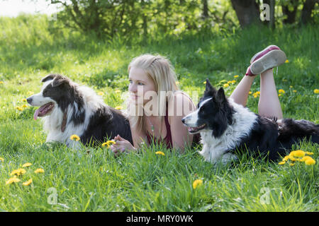 Vista laterale del sorridente giovane donna bionda che giace tra due Border Collies cani all'esterno. La donna e i cani sono guardando in avanti. Foto Stock