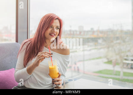 Bella ragazza seduta in una caffetteria. Giovane donna godere nella giornata di sole. Ritratto di pretty redhead girl indoor. Foto Stock