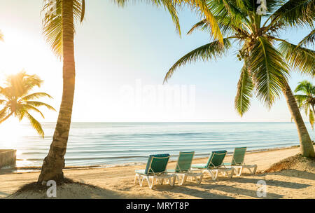 Spiaggia Tropicale scena di vacanza con palme e sedie a sdraio sotto la sabbia dall'acqua Foto Stock