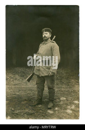 German Historical foto: un soldato con una birra belly in uniforme militare in piena marcia con un fucile sulla sua spalla in posa all'esterno. la prima guerra mondiale Foto Stock