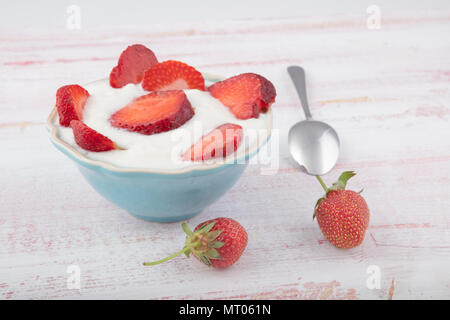 Fresche succose fragole con yogurt biologici in ceramica blu ciotola sul tavolo di legno, fuoco selettivo Foto Stock