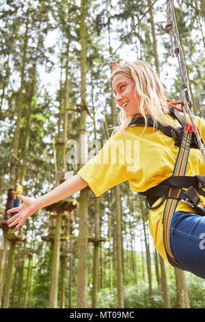 Giovane donna nella foresta di arrampicata o corde alte corso mentre rappelling su un corso di arrampicata Foto Stock