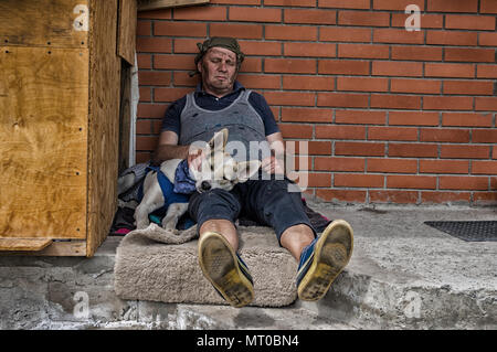 Due senzatetto fiends - uomo e cane dorme seduto su una concreta contro un muro di mattoni Foto Stock