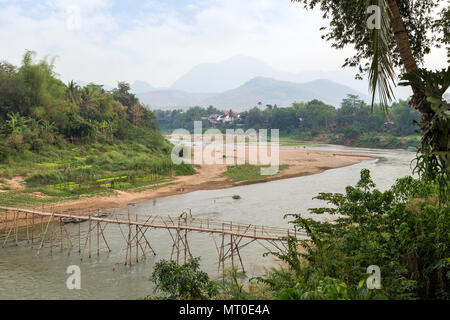 Vista di un bambù ponte sul fiume Nam Khan a bassa marea e lussureggianti riverbank a Luang Prabang, Laos, in una giornata di sole. Foto Stock