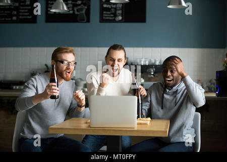 Multirazziale uomini di bere birra celebrando la vittoria la visione di gioco Foto Stock