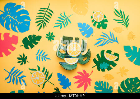 Ceramica foglia di monstera in intestazione tropicale con le arance, foglie e frutti pattern su un giallo brillante background. Piatti colorati laici carta con ritagli. Foto Stock