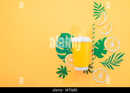 Carta monouso cup su sfondo giallo con foglie tropicali e fettine di arancia su un brillante sfondo giallo. Colorata bevanda estiva concetto con p Foto Stock