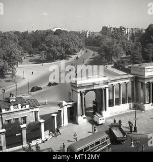 Degli anni Cinquanta, storico, veicoli passando attraverso i cancelli a Hyde Park Corner, l'ingresso di Hyde Park, uno dei parchi reali, Knightsbridge, Londra, Inghilterra, Regno Unito. In lontananza si vede il famoso Park Lane. Il parco è stato istituito da Enrico VIII 1536 per essere utilizzato come terreno di caccia e fu aperta al pubblico nel 1637. Foto Stock