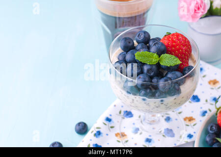 Un bicchiere di caffè e budino chia con mirtilli e fragole per la colazione. Cibo vegetariano. Sfondo blu. Tovagliolo con fiori. Colori luminosi. Foto Stock