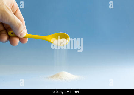 Giallo cucchiaio zucchero ruotando su sfondo blu Foto Stock