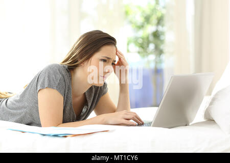 Preoccupati i lavoratori autonomi alla scoperta di errore online lavorando su un letto di casa Foto Stock