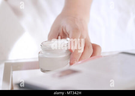 Donna di mano sollevare il craem jar sul tavolo Foto Stock