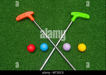 Due mini golf putters sono attraversati con colorati mini palline da golf sul green in erba sintetica Foto Stock