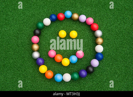 Faccia felice formata con colorati mini palline da golf su erba artificiale Foto Stock