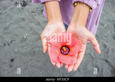 Ragazza asiatica indossare un bracciale oro permanente sulla sabbia Holding Peach colore dei fiori sul palmo della mano Foto Stock