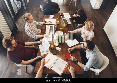 Gruppo di collaboratori creativi sedersi attorno a un tavolo di legno in uno spazio aperto e funziona con la documentazione aziendale e laptop. Concetto di lavoro nell'offic Foto Stock