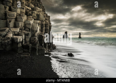 Reynisfjara famosa spiaggia nera con le colonne di basalto e il mare Reynisdrangar pile. Foto Stock