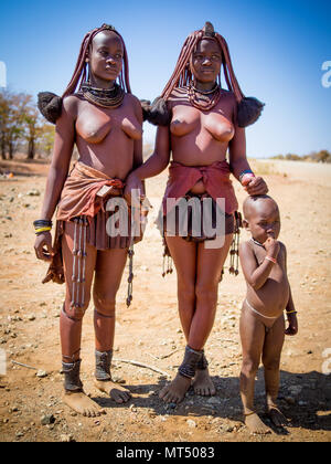 Opuwo, Namibia - Luglio 25, 2015: Ritratto di unidentified le donne himba in piedi con ragazzo nel deserto Foto Stock