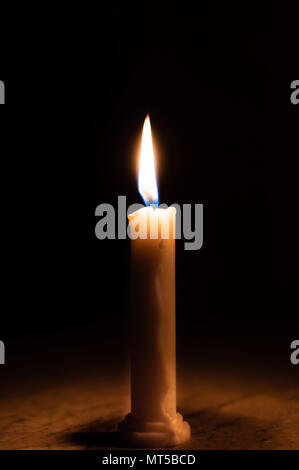 Un tavolo illuminato da una candela in una stanza buia Foto Stock