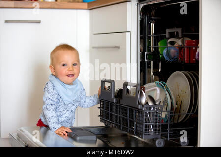 Bimbo piccolo bambino, ragazzo, aiutando la mamma, mettendo i piatti sporchi nella lavastoviglie a casa, cucina moderna Foto Stock