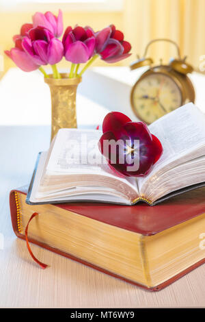La Santa Bibbia e oro antico orologio sveglia con fiori sul tavolo di legno dello sfondo. Foto Stock