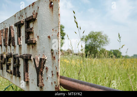 Close-up, immagine astratta di una parte di un metallo di proprietà privata segno attaccato ad un bloccato fattoria. Erba di Prato può essere visto in background. Foto Stock