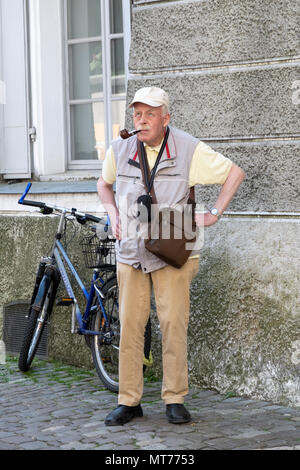 Un turista con una fotocamera e un sacchetto di uomo di fumare un tubo su una strada laterale a Regensburg, Germania Foto Stock