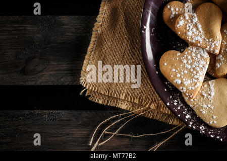 Deliziosa fatta in casa a forma di cuore i cookie spolverati con zucchero a velo su un letto di sacco e di tavole di legno. L'immagine orizzontale visto da sopra. Foto Stock