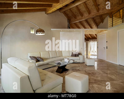 Soggiorno interno in primo piano il beige divano in pelle e la tabella di caffè di vetro con arco lampada da terra il soffitto in travi di legno esposte Foto Stock