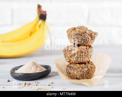 Una sana senza glutine homemmade muffin alla banana con farina di grano saraceno. Pila di tre vegane muffin con semi di papavero su grigio tavolo in legno. Spazio di copia Foto Stock