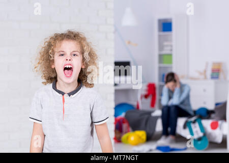 Scuola ragazzo gridando, madre che copre le sue orecchie in background Foto Stock