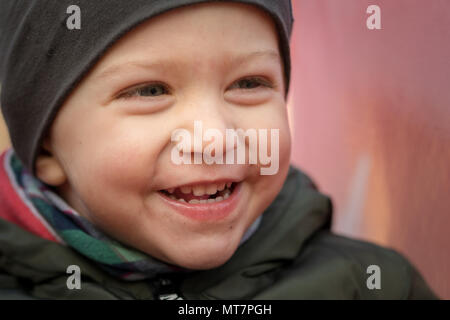 Happy baby boy con un cappuccio ridevano forte seduto su una slitta per bambini,vicino. Foto Stock