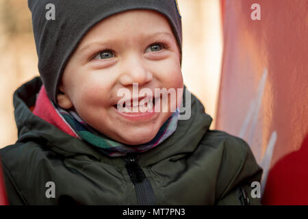 Felice ragazzino con un cappuccio ridevano forte seduto su una slitta per bambini,vicino. Foto Stock