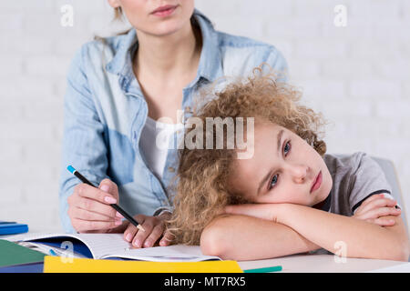 Annoiato ragazzo appoggiato la testa sulle sue braccia mentre si fanno i compiti Foto Stock