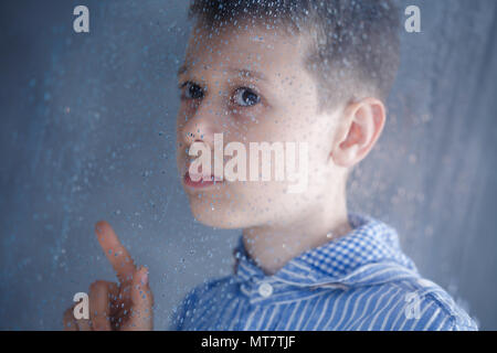 Triste ragazzo dietro la finestra in un giorno di pioggia Foto Stock