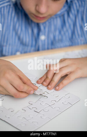 Focalizzato boy risolvere un puzzle su un tavolo Foto Stock