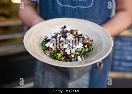 Primo piano di un server che indossa un grembiule in piedi al di fuori di un bistro con in mano una coppa con una deliziosa insalata mista Foto Stock