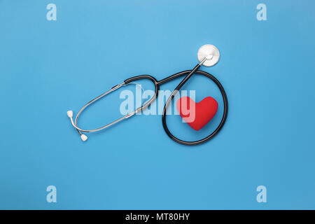 Table top visualizza immagine aerea di accessori del settore sanitario e medico di fondo concetto.cuore rosso & stetoscopio su carta blu.Flat laici gli elementi essenziali per Foto Stock