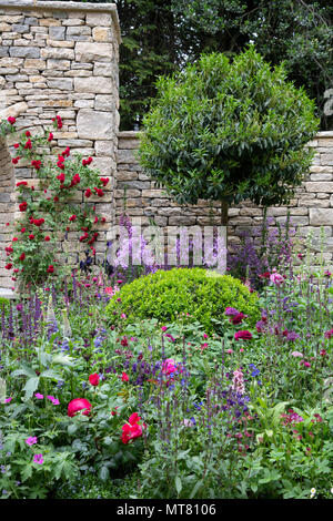 Un secco di nicchia in pietra circondato da multi-piante colorate nelle rivendicazioni ragazzi-molto giardino inglese della RHS Chelsea Flower Show 2018, London, Regno Unito Foto Stock