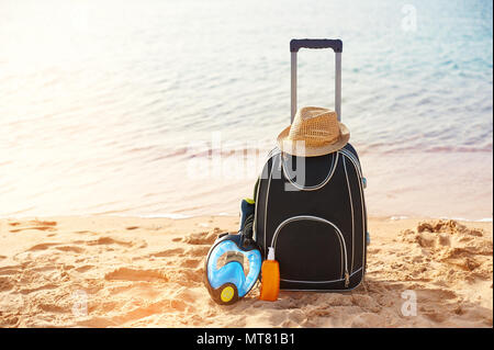 Valigia e cappello, crema solare con una maschera. Il mare tropicale, spiaggia in background. Il concetto di ricreazione di estate viaggi e traffico crocieristico Foto Stock