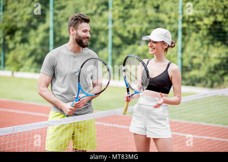 Coppia giovane divertendosi in piedi sul campo da tennis Foto Stock