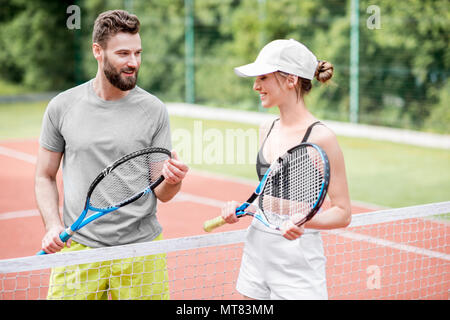 Coppia giovane divertendosi in piedi sul campo da tennis Foto Stock