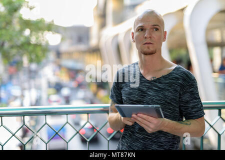 Bel giovane uomo calvo pensando tenendo tavoletta digitale su Foto Stock