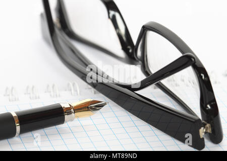 Primo piano della penna stilografica e occhiali neri giacente su aprire il notebook a spirale Foto Stock