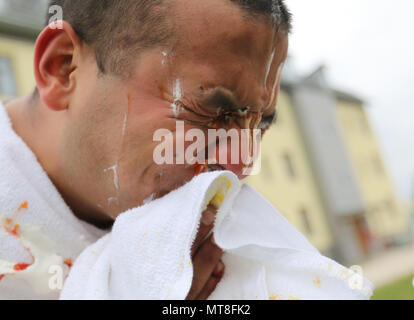 Sgt. Issac Gonzalez, operazioni sottufficiale assegnato al settimo esercito Comando di formazione presso la sede centrale e sede società, rimuove i resti di una panna montata, la senape e il ketchup torta dal suo volto in Graffenwoehr, Germania, 11 maggio 2018. Soldati dal 7ATC ha condotto un grafico a torta-in--faccia caso a raccogliere fondi per l'esercito di soccorso in caso di emergenza la campagna. Finora la manifestazione ha raisied oltre 400 dollari in un'ora. (U.S. Esercito foto di Sgt. Marlon Stili) Foto Stock