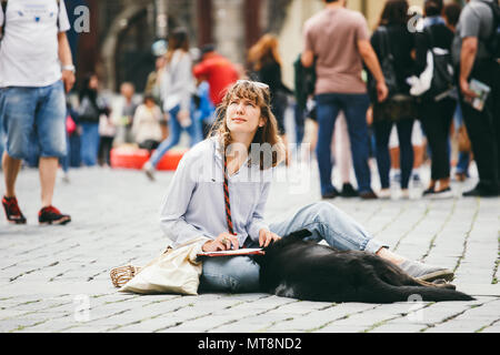 Repubblica Ceca, Praga, luglio 25, 2017: una giovane e bella donna pittore si siede sul pavimento al centro della piazza e richiama, accanto a lei si trova un blac Foto Stock